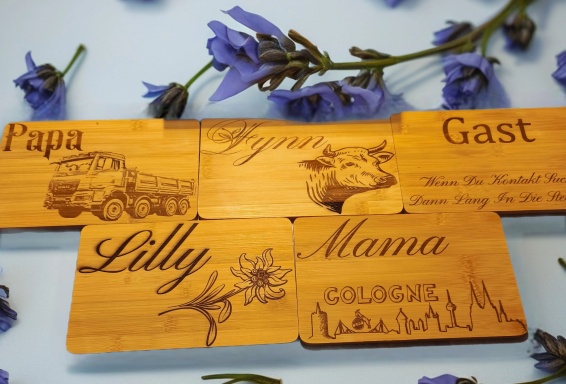 Gravierte Holzschilder mit den Namen Papa, Mama, Lilly, Gast und einem Kuhmotiv.